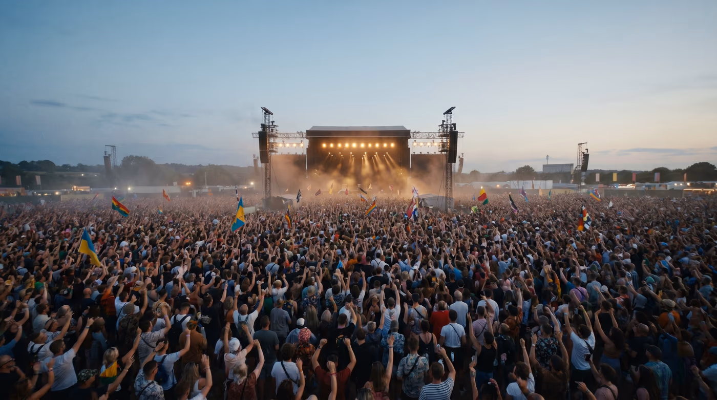 Foule immense devant une grande scène de festival au coucher du soleil, drapeaux levés